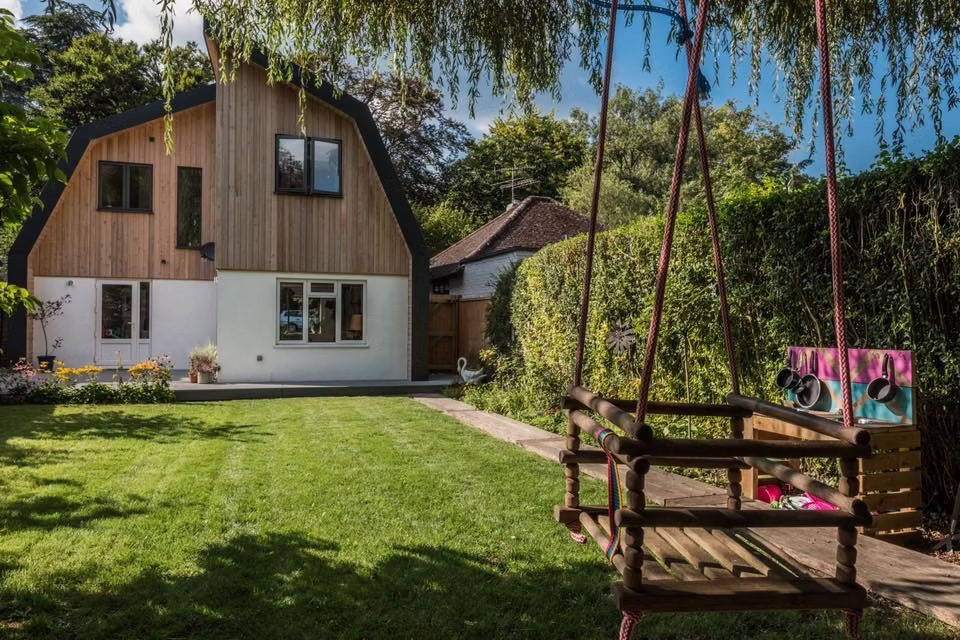 The Nook transforms a dated 1950s bungalow in Forest Row into a contemporary Dutch barn-inspired family home. Rather than extending outwards, the design reworks the existing roof form to create a full first floor within the original footprint, preserving the garden and neighbouring views.