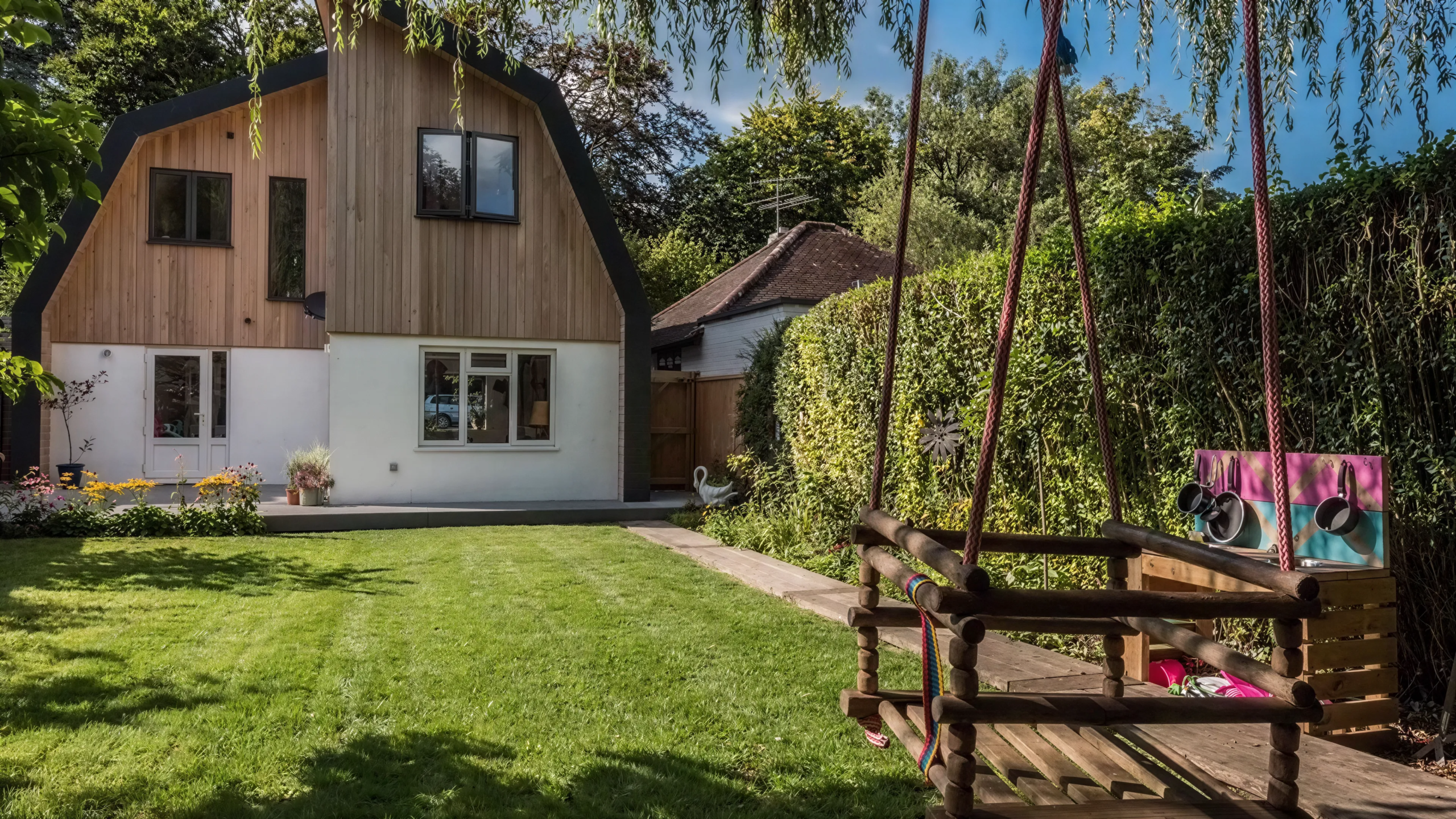 Rear elevation of a Dutch barn-style home conversion with larch cladding overlooking a landscaped family garden.
